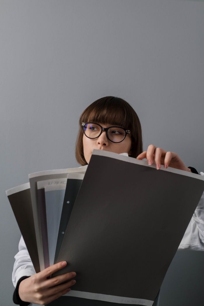 about-01 A woman wearing glasses examines various paper samples, offering a minimalistic and modern aesthetic.